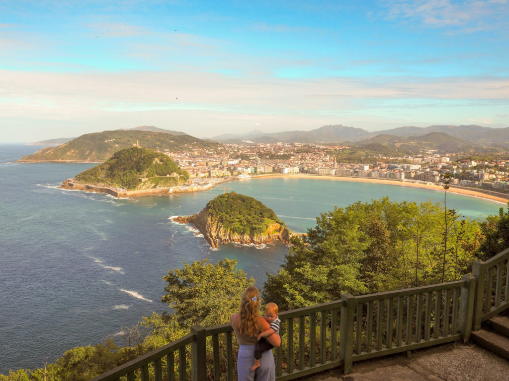 Mother holding a baby looking out from a viewpoint over the crescent-shaped bay at San Sebastian, Spain