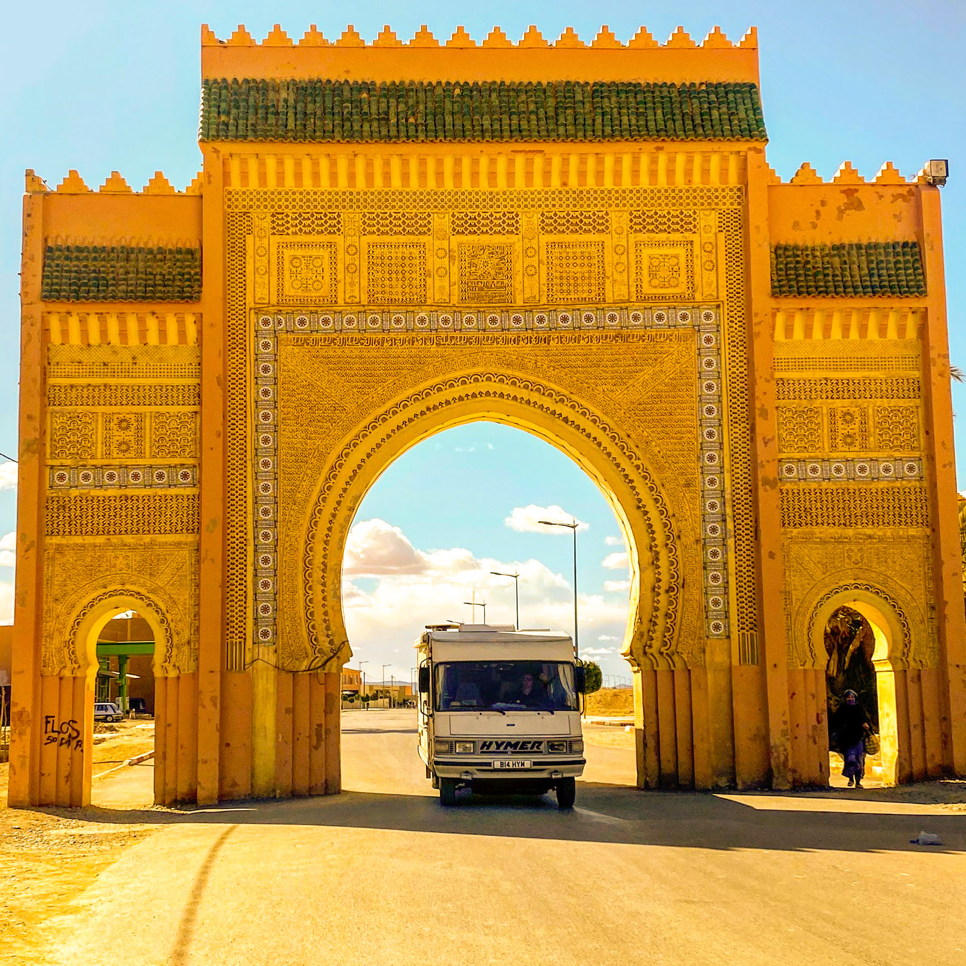 Classic Hymer motorhome driving through ornate entrance gate at the town of Tazzarine, Morocco