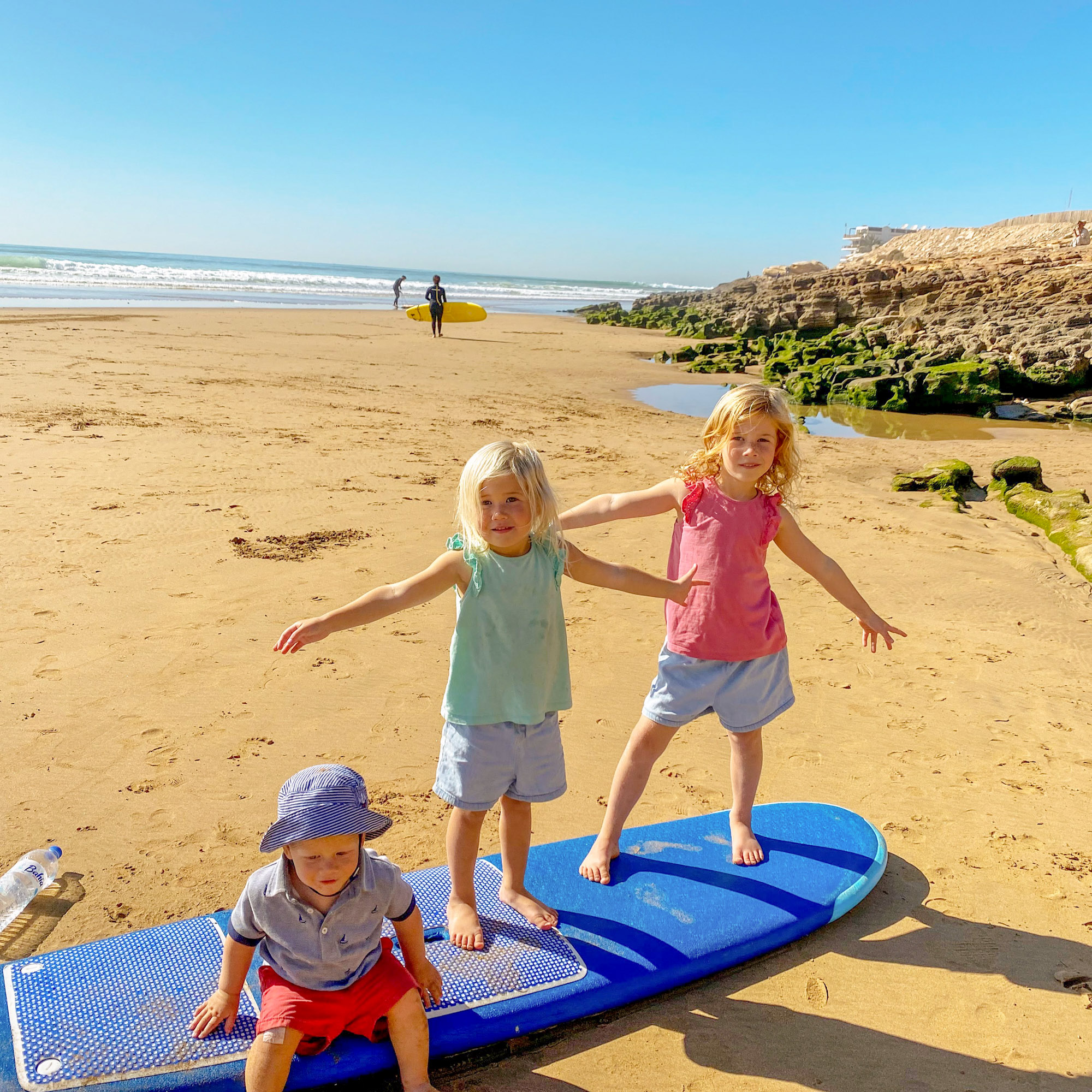 3 small children standing on a surfboard on the beach at Taghazout, Morocco