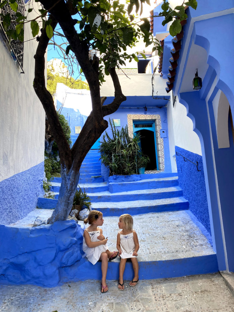 2 small girls sat on a step in the blue town of Chefchaoun, Morocco