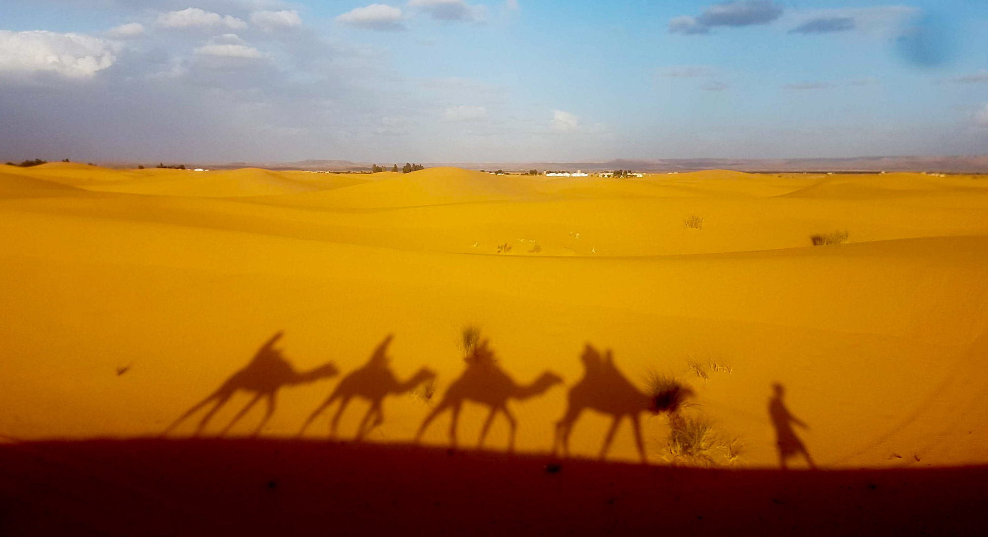 Shadow of a group riding camels in the desert at Merzouga, Morocco