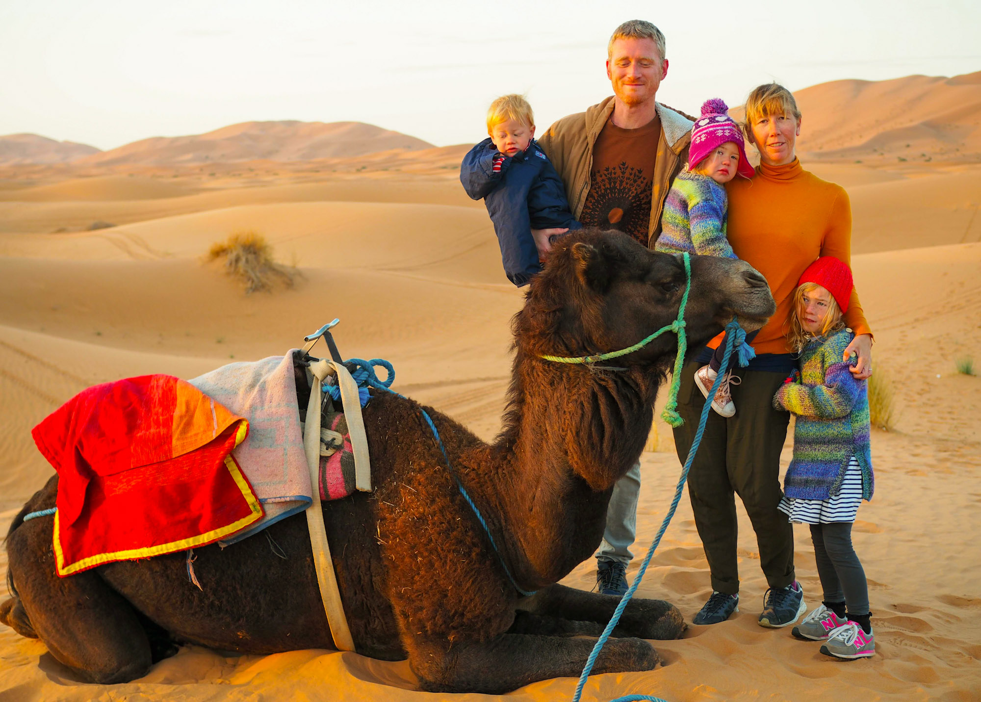 Family with small children stood next to a camel in the Sahara Desert