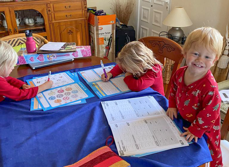 3 young children sat at a table, writing in workbooks