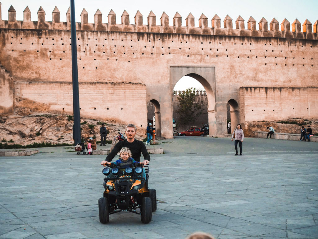 Man and daughter riding an electric quad bike together outside the city walls in Fes, Morocco