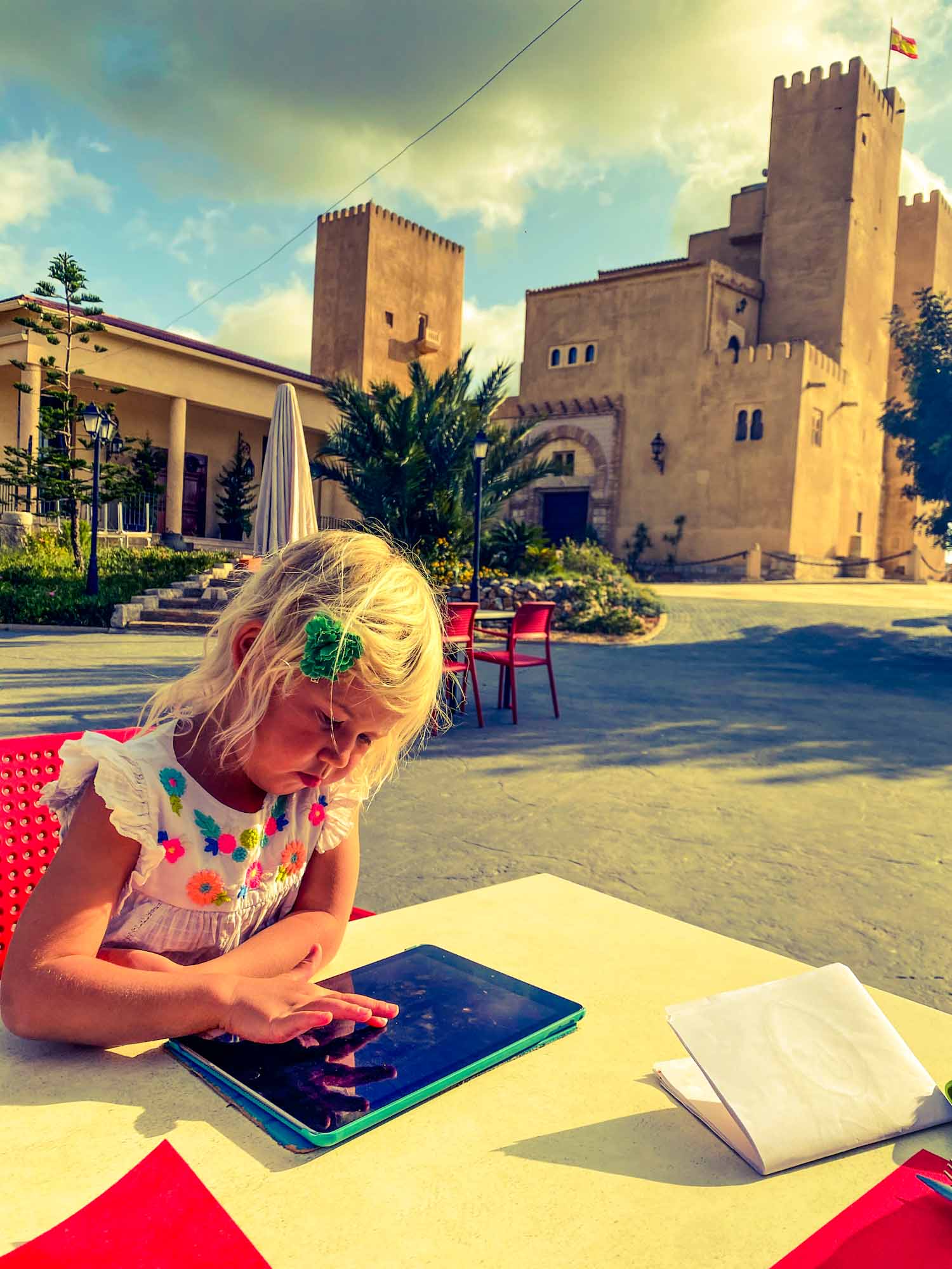 Young girl using an ipad while sat at a restaurant table, with castle behind