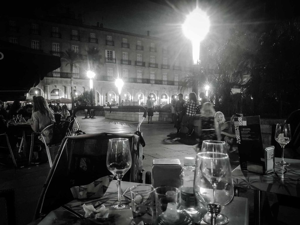 Wine glasses on a cafe table at night, overlooking the Plaza Nueva square in Bilbao, Spain