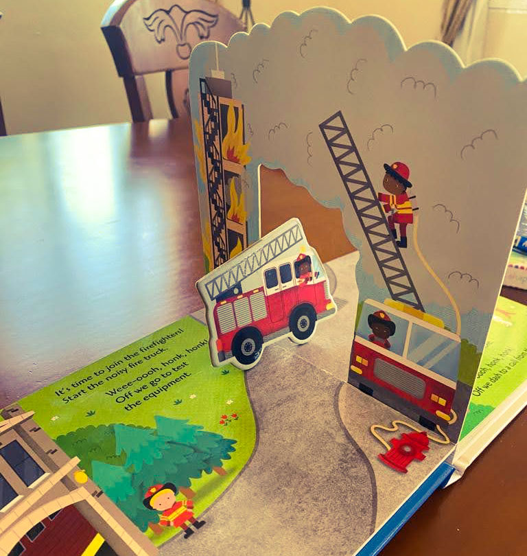 View inside a colourful children's book, with pop-up scenes and a fire engine