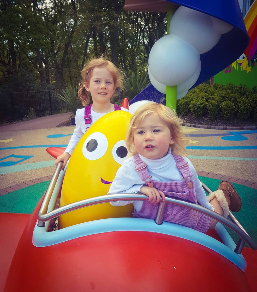 2 small girls sat in a colourful play aeroplane, outside the CBeebies Land Hotel at Alton Towers