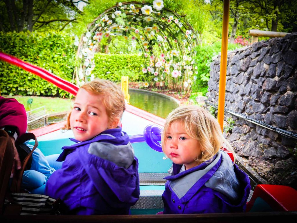 2 small girls riding under an archway of flowers on a theme park boat ride