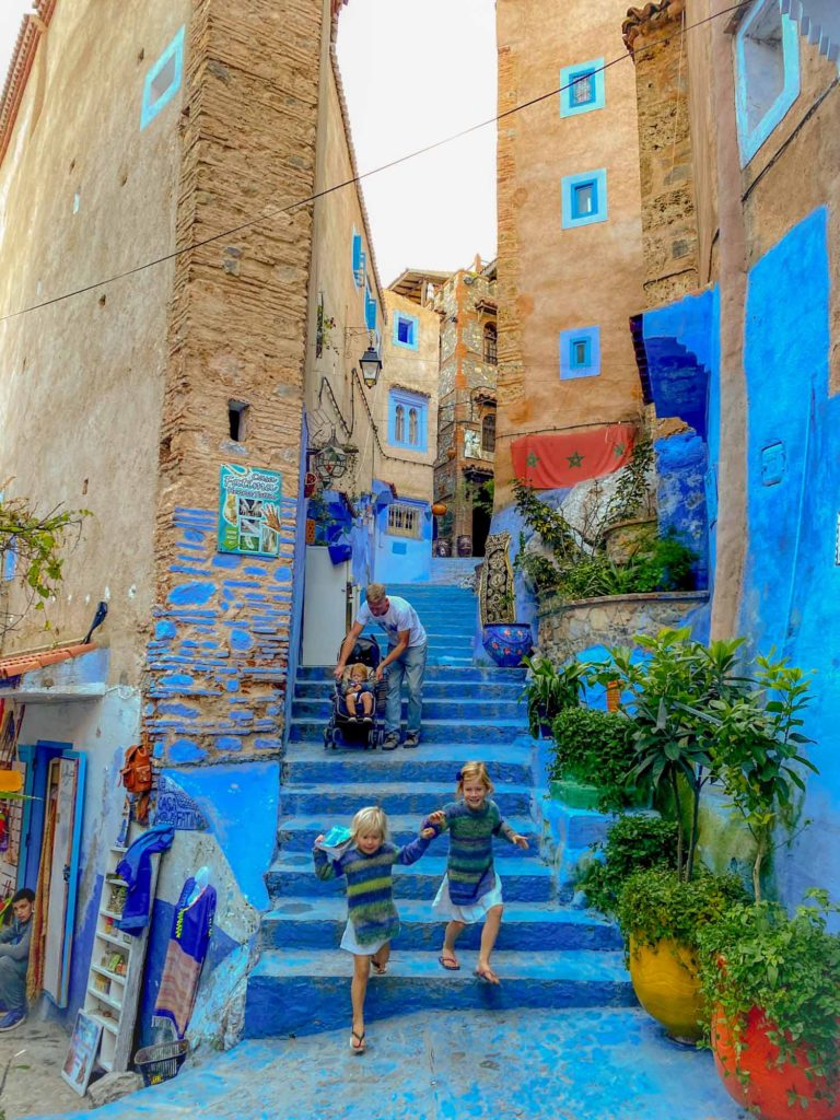 Father with 3 small children (1 in a pushchair) descending some painted blue stairs in Chefchaoun, Morocco