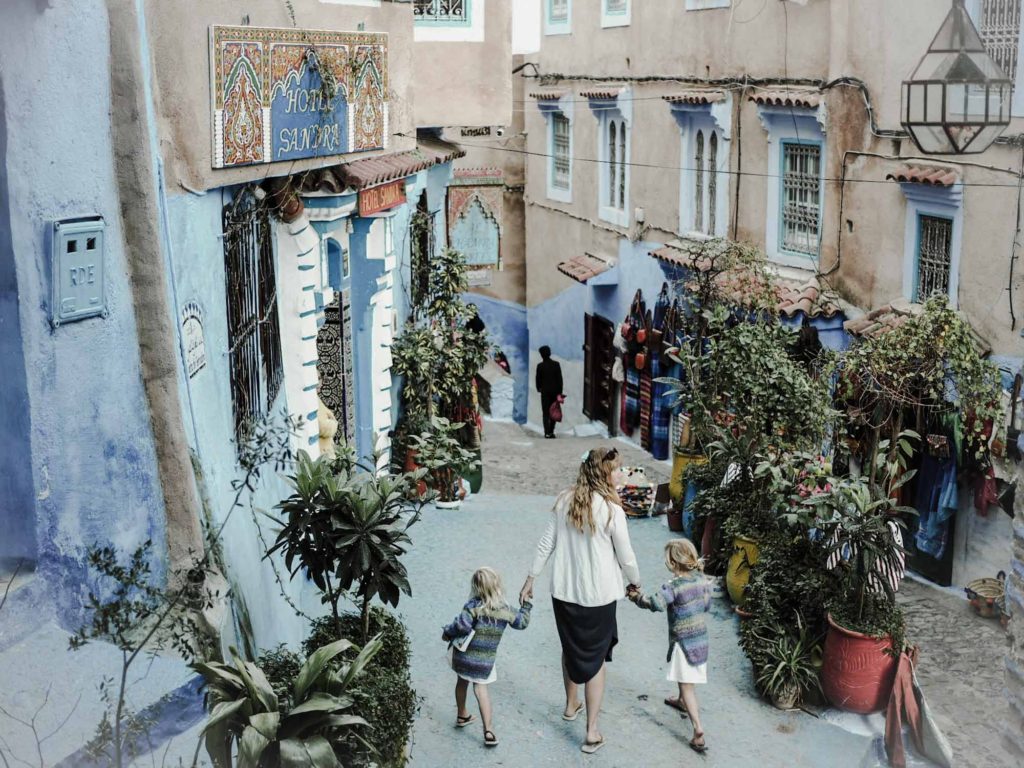 Mother and 2 small daughters walking down a pretty blue painted street, lined with pot plants, in Chefchaoun, Morocco