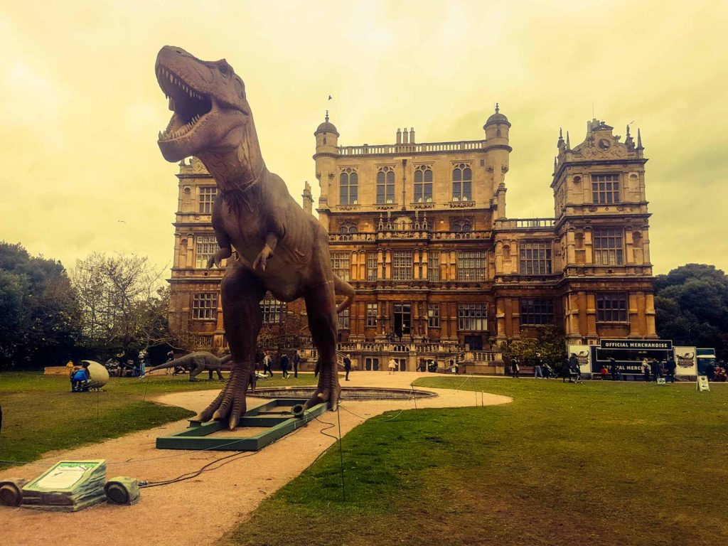 A life-size tyrannosaurus rex model dinosaur, stood in front of Wollaton Hall in Nottingham