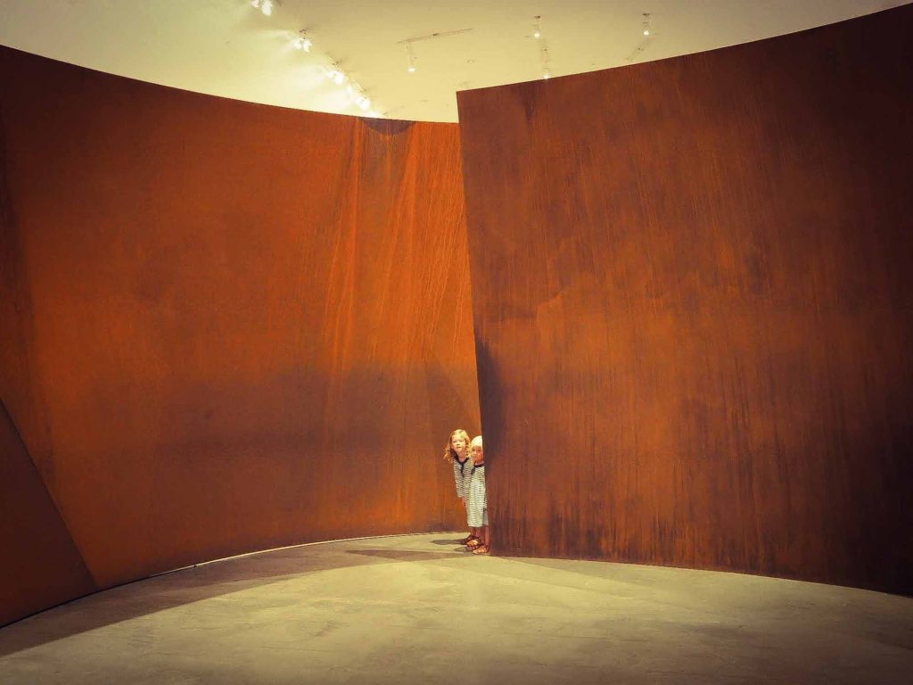 2 small girls peeping around a corner inside a giant brown metal artwork in the Guggenheim Museum, Bilbao
