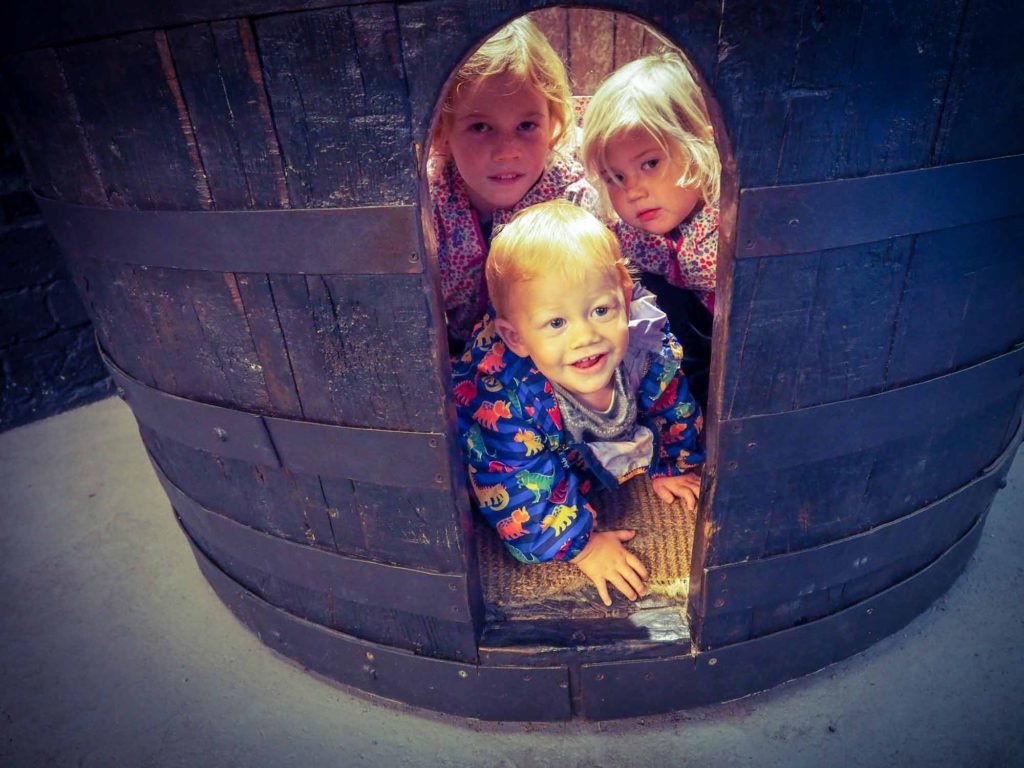 3 small children peeping out of a carved hole in the side of an ornamental port wine barrel