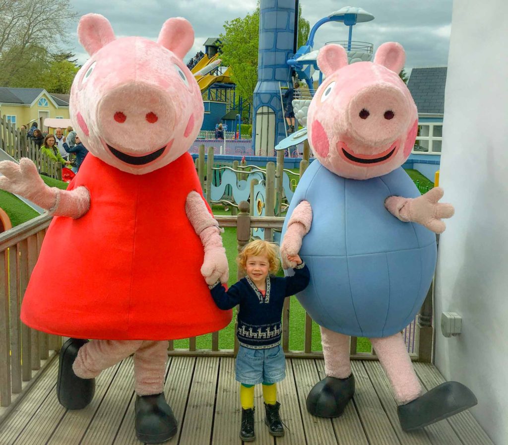 Young girl holding hands with some large costumed characters dressed as Peppa and George, from 'Peppa Pig'