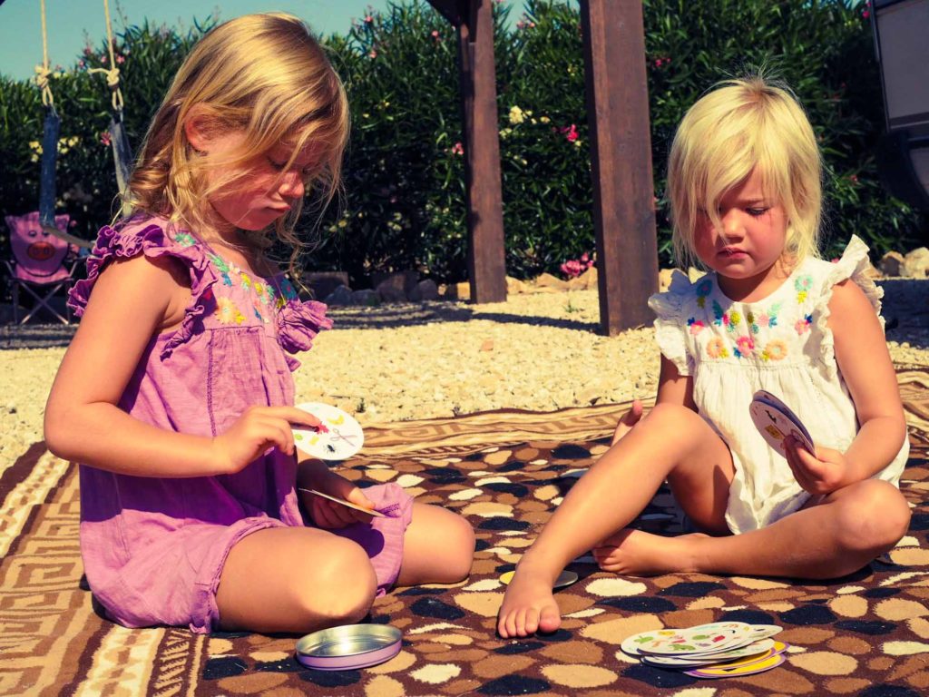 2 young girls sat on the floor outside on a rug, playing the card game 'Dobble'