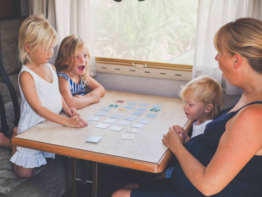 Family with small children sat around a table inside a motorhome, playing a pairs memory game