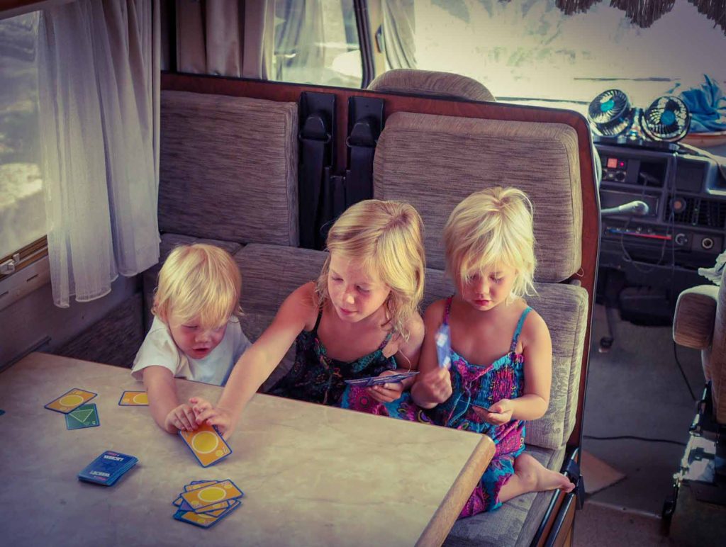 3 small children sat at a table inside a motorhome, playing the card game, 'Whot!'