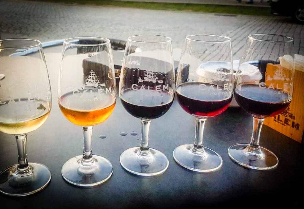 5 glasses of different coloured port wine, lined up along a table for a port tasting, in Porto