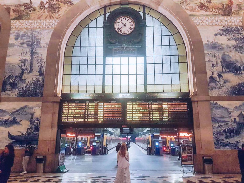 Lady stood looking at the illuminated departures board, flanked by tiled frescoes, inside the beautiful Sao Bento train station in Porto