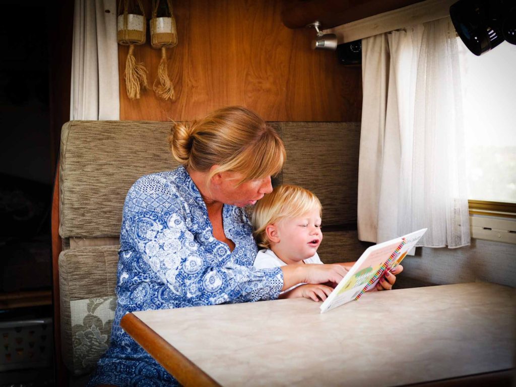 Mother and baby boy sat at a table in a motorhome, reading a book together