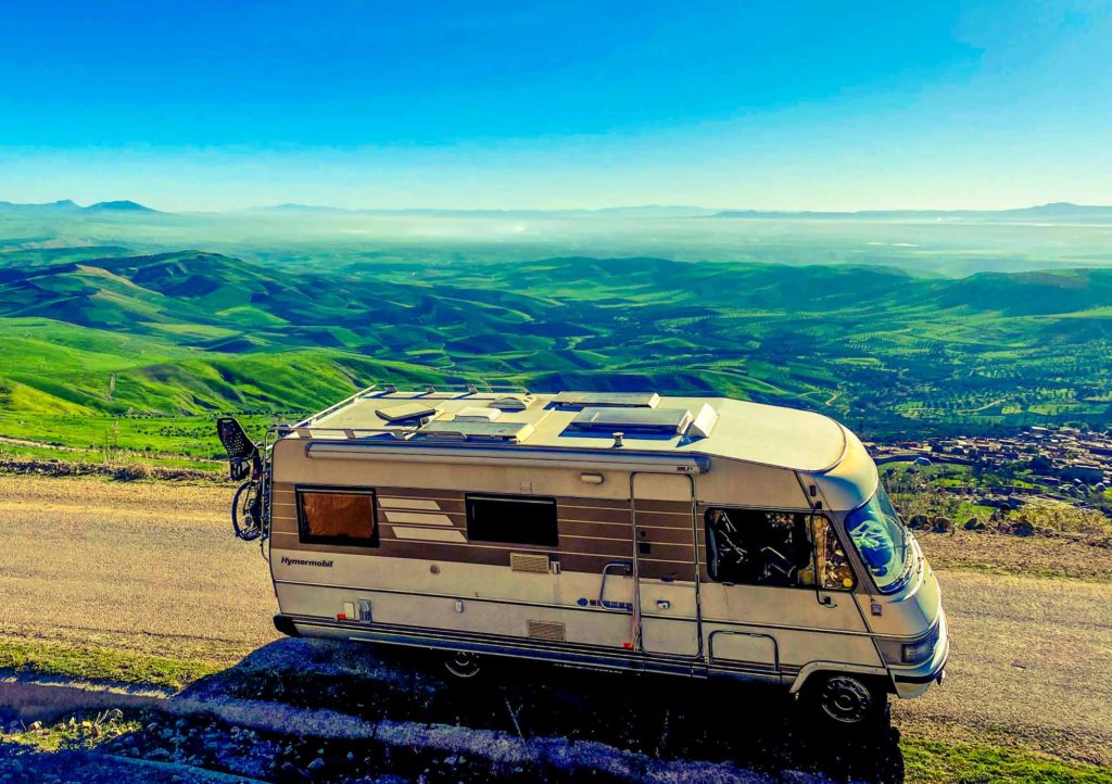 Classic Hymer motorhome at a viewpoint in the Rif Mountains, Morocco, with an expansive view of rolling green hills behind.