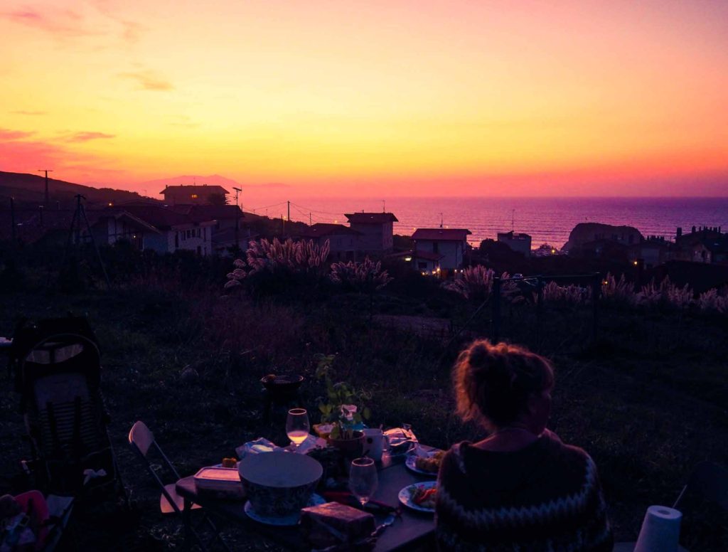 Lady eating dinner at a camping table with a view of a sunset over the sea, in Sopelana, Basque Country, Spain