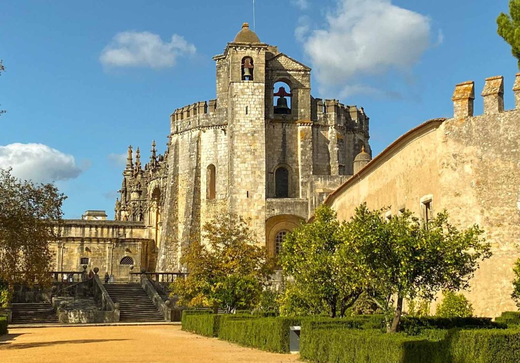 Stone exterior of a circular church, with formal gardens in front, at the Convent of Christ, Tomar