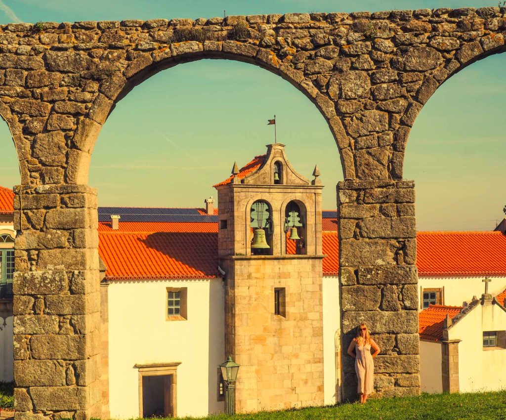 Lady stood in front of a stone arch, part of the historic aqueduct in Vila do Conde, Portugal, with monastery behind