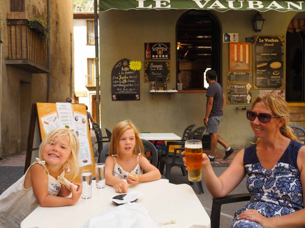 Mother and 2 small children sat enjoying a drink at an outdoor cafe table, in Villefranche-de-Conflent, France