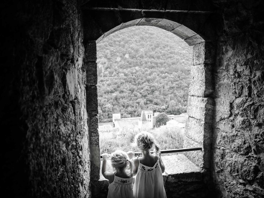 2 small girls stood at a stone viewing window, overlooking the town of Villefranche-de-Conflent, France