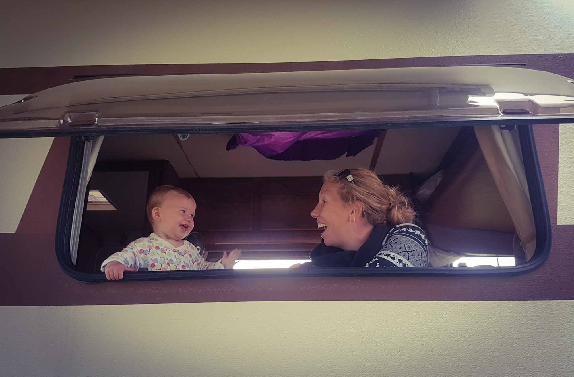 Mother and baby both looking out of a motorhome side window and smiling