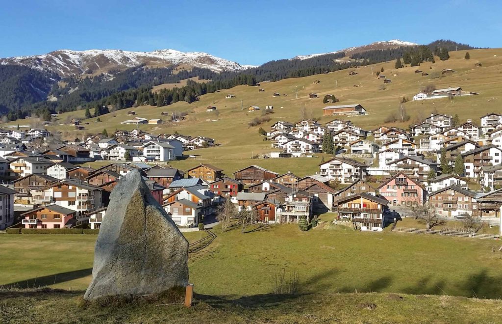View of traditional wooden chalets in the mountain village of Falera, Switzerland, with standing stone in the foreground