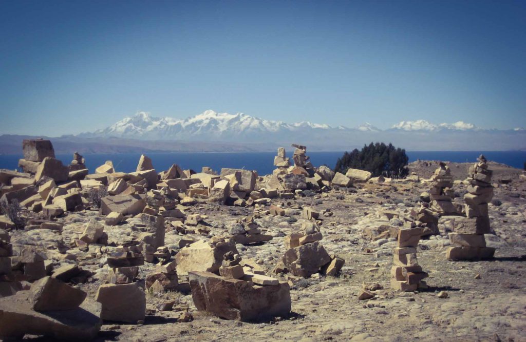 A collection of constructed rock towers, at a viewpoint overlooking water and snowy mountains behind