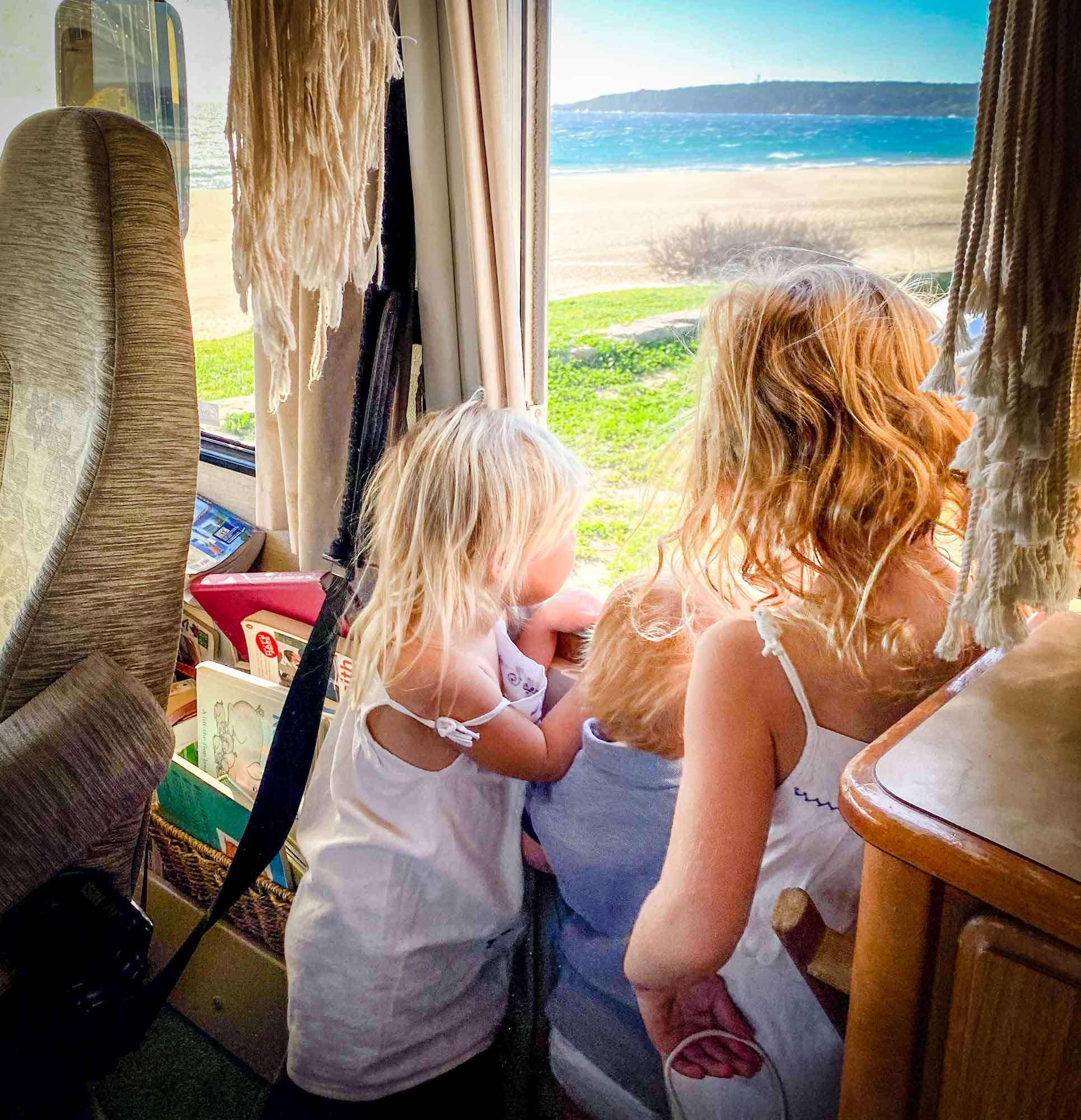 3 small children looking out of a motorhome window at a beach