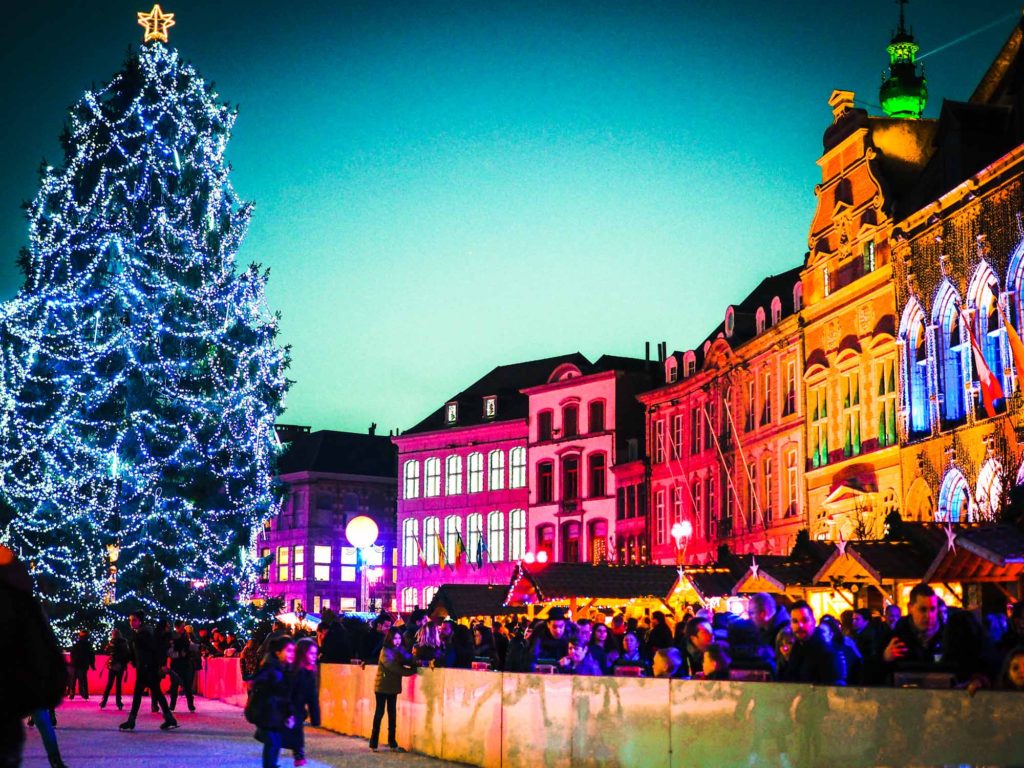 Outdoor ice rink with giant Christmas tree, market stalls and illuminated houses behind
