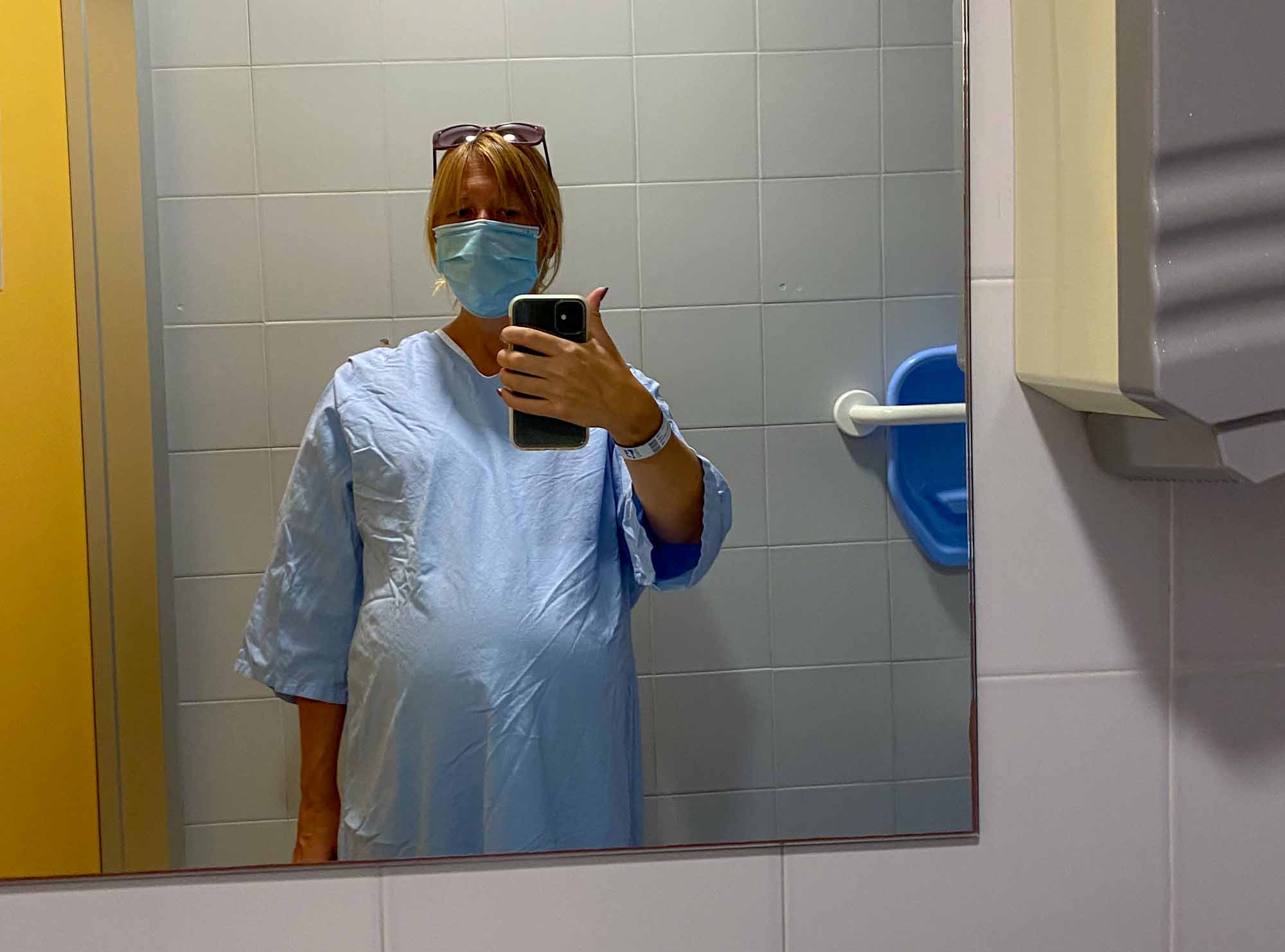 Pregnant lady wearing a face mask, taking a picture of herself in the mirror