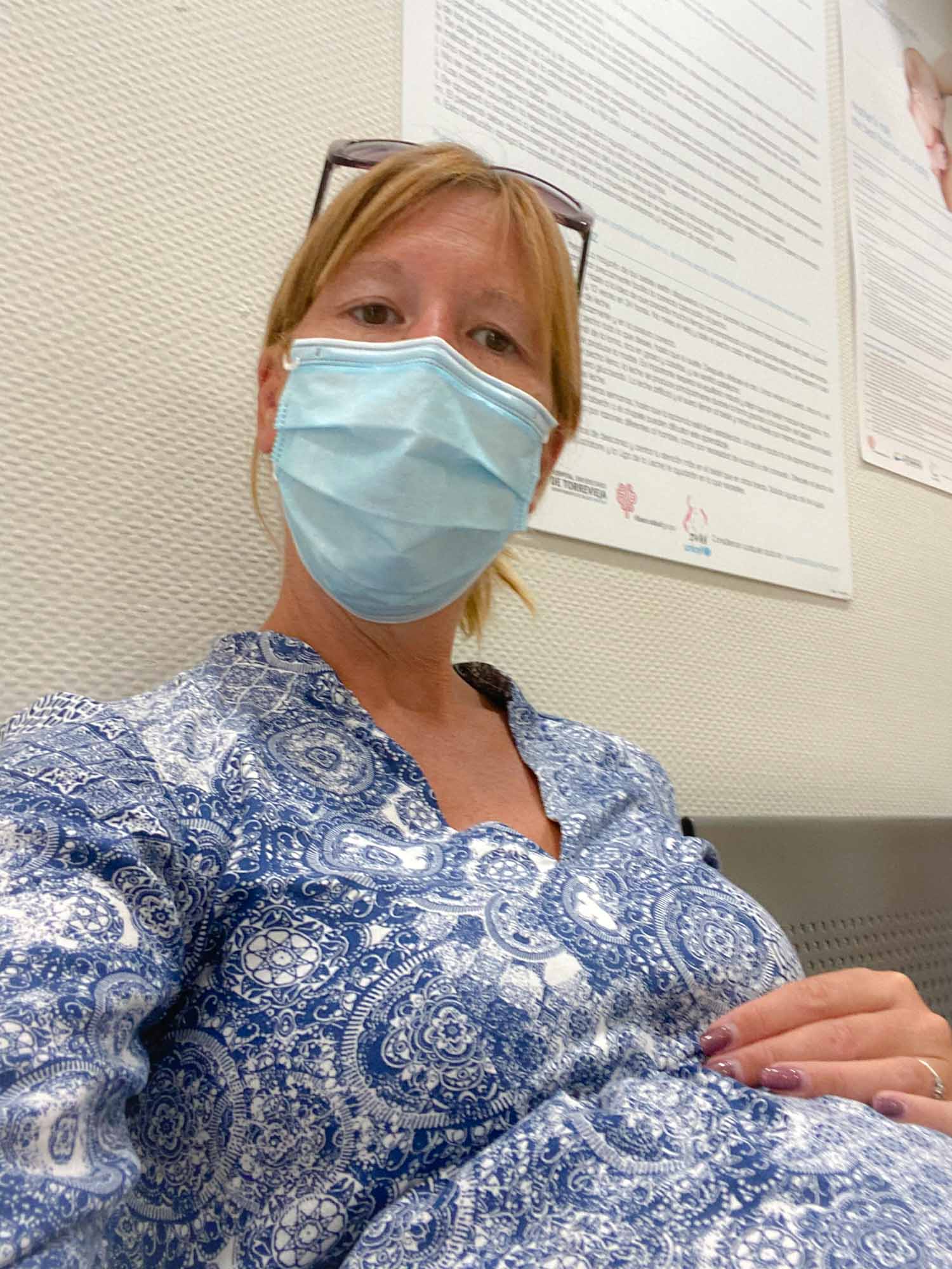 A pregnant woman sat wearing a medical facemask
