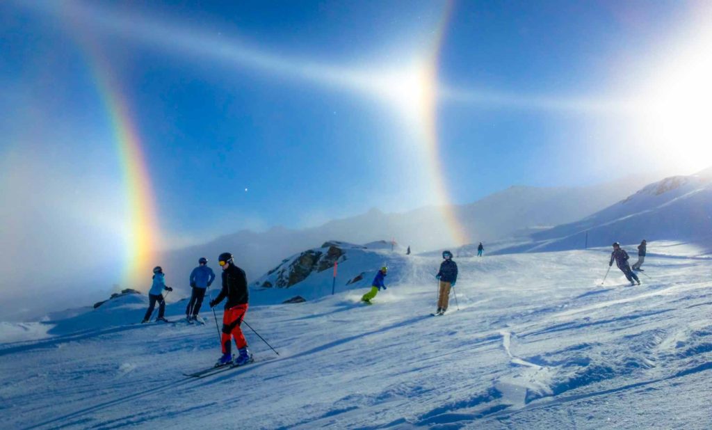 Snowy ski slope, with incredible rainbows above caused by ice crystals in the air