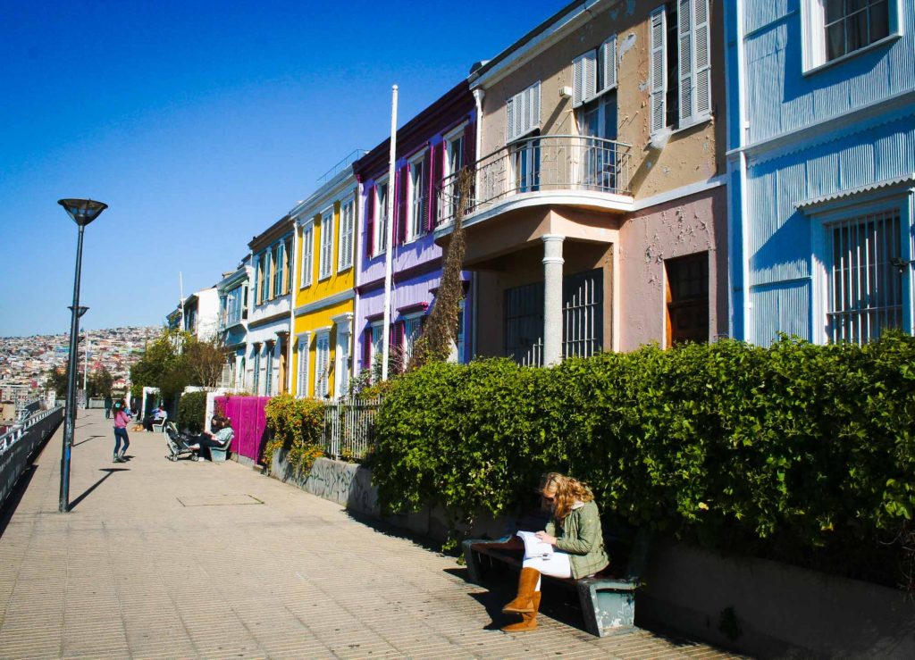 Lady sat on a bench in front of a row of colourful houses
