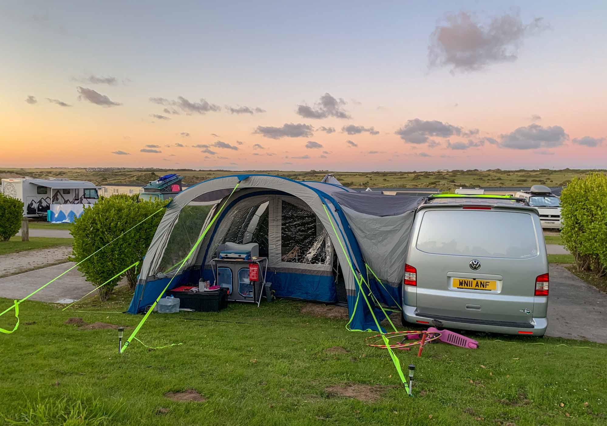 A VW Transporter campervan, with side awning tent attached, parked at a campsite, at sunset