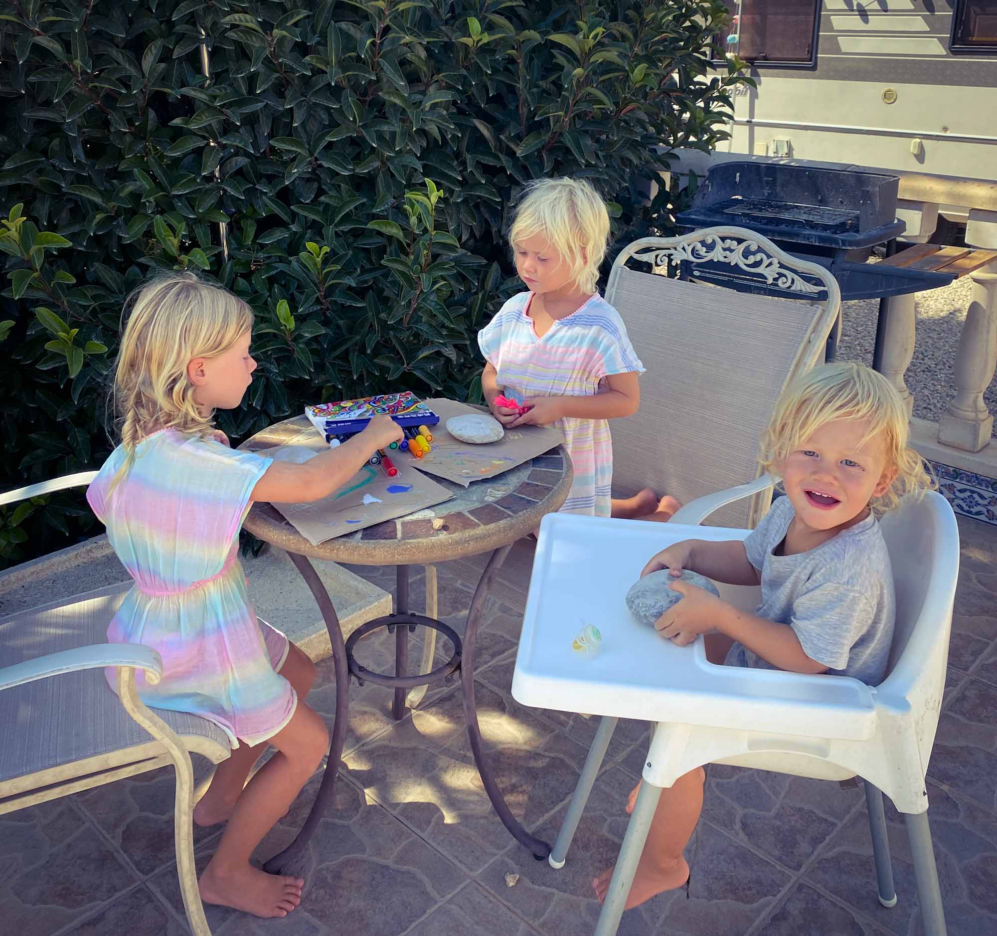 3 children sat at an outside garden table, painting stones with paint pens