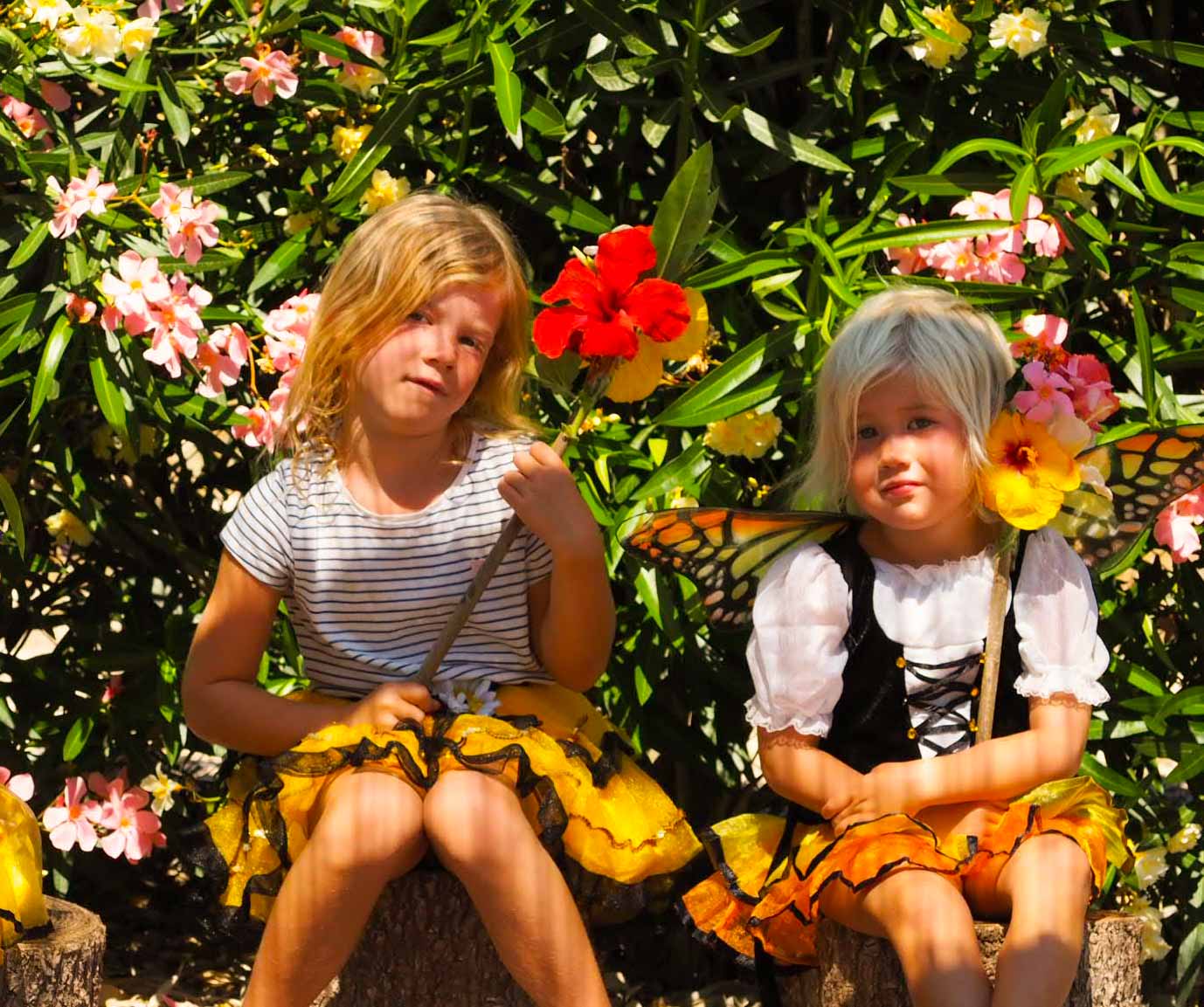 2 girls dressed in bee and butterfly costumes holding handmade wands made from sticks and flowers