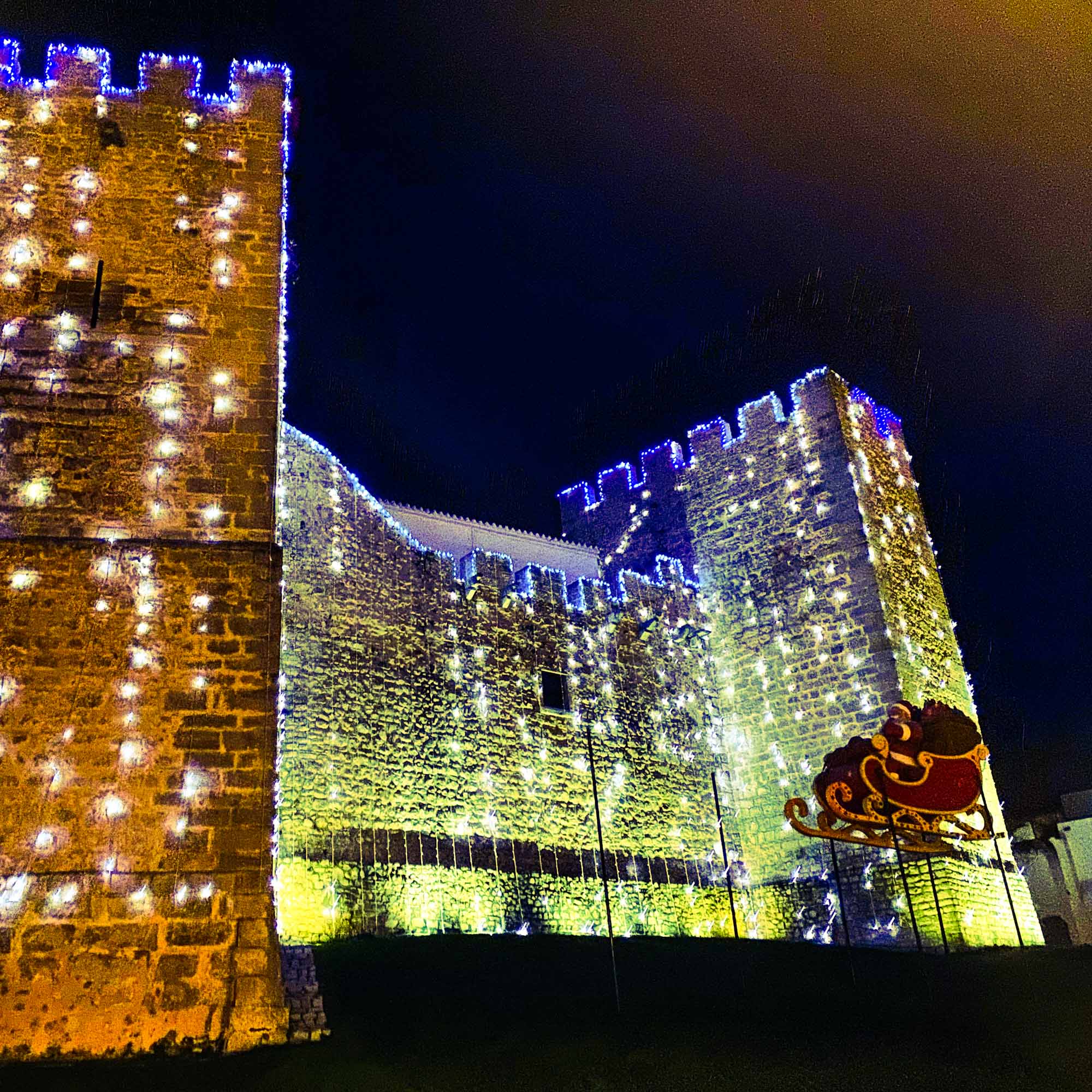 High stone outer wall of Loule Castle, Portugal, illuminated with Christmas string lights