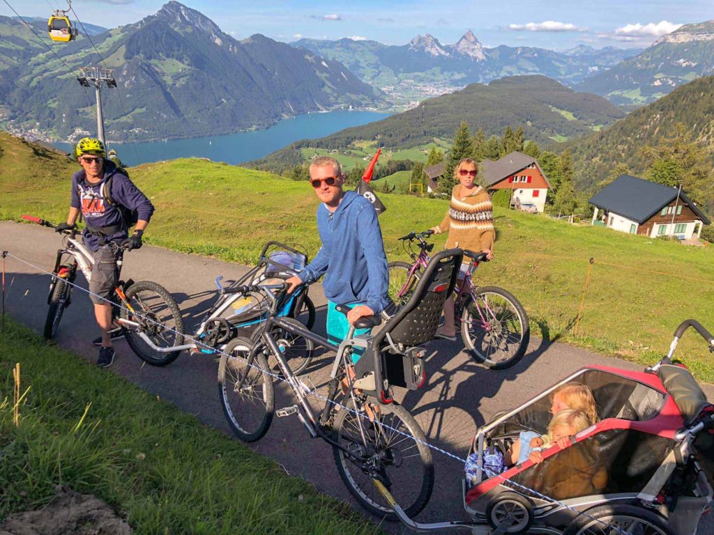 Group bike ride in the Swiss Alps with mountain views, with children in a bike trailer