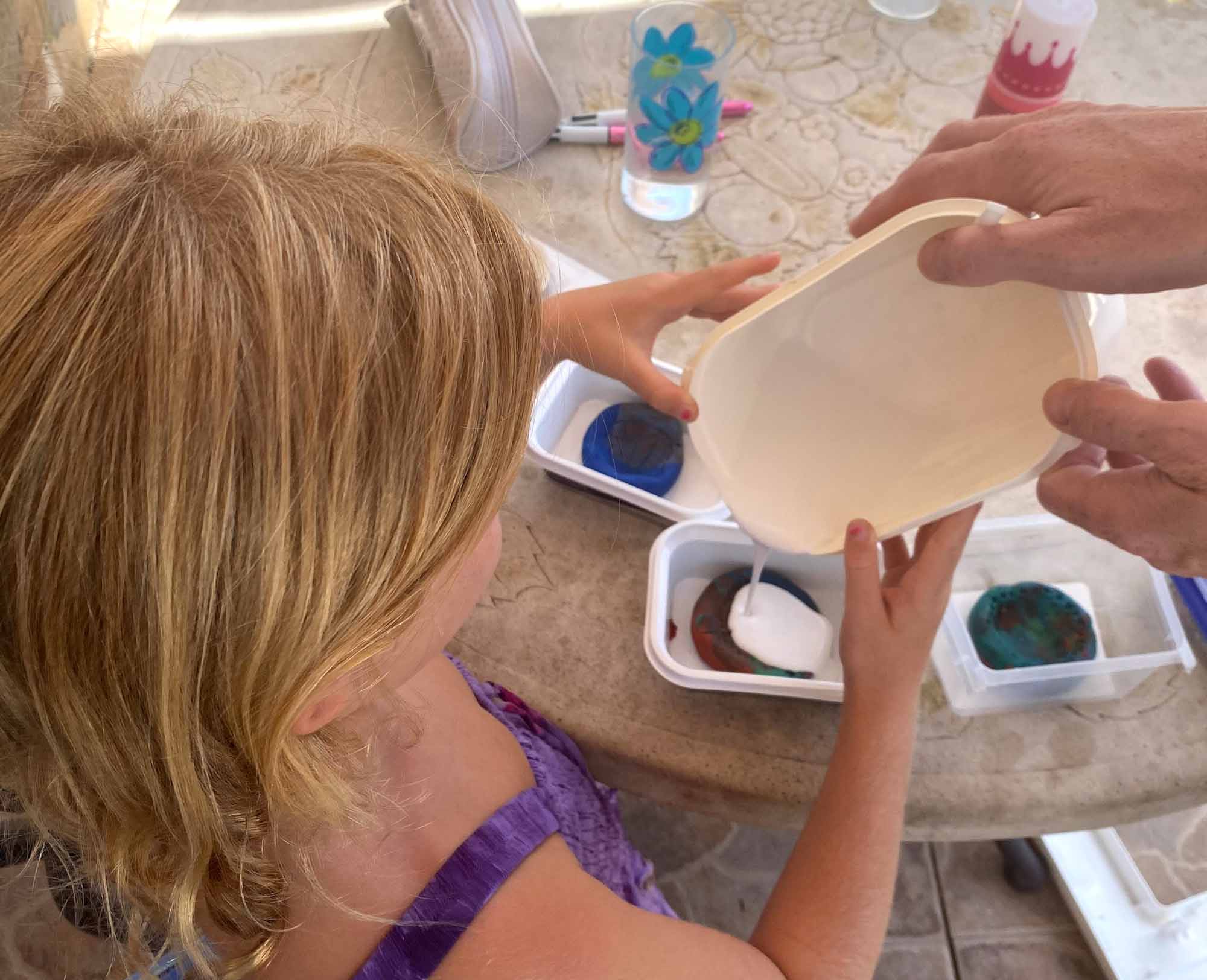 Girl pouring plaster of paris into a plastacine mould, with the help of an adult