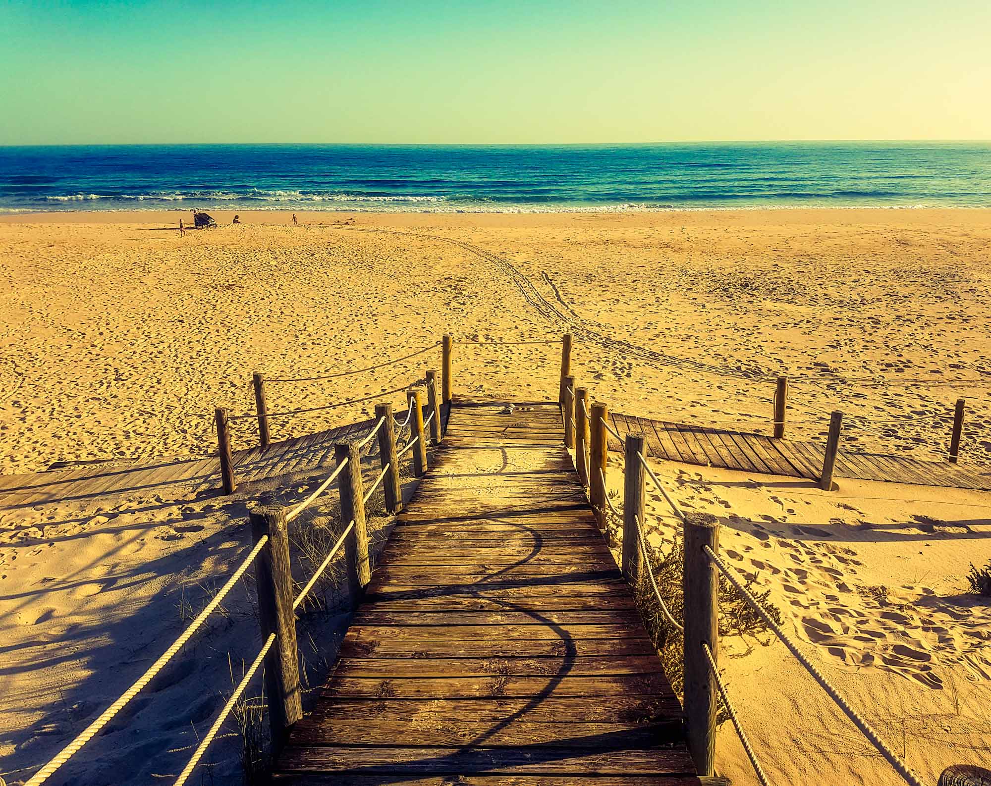 Looking down a wooden boardwalk leading onto a large, empty sandy beach