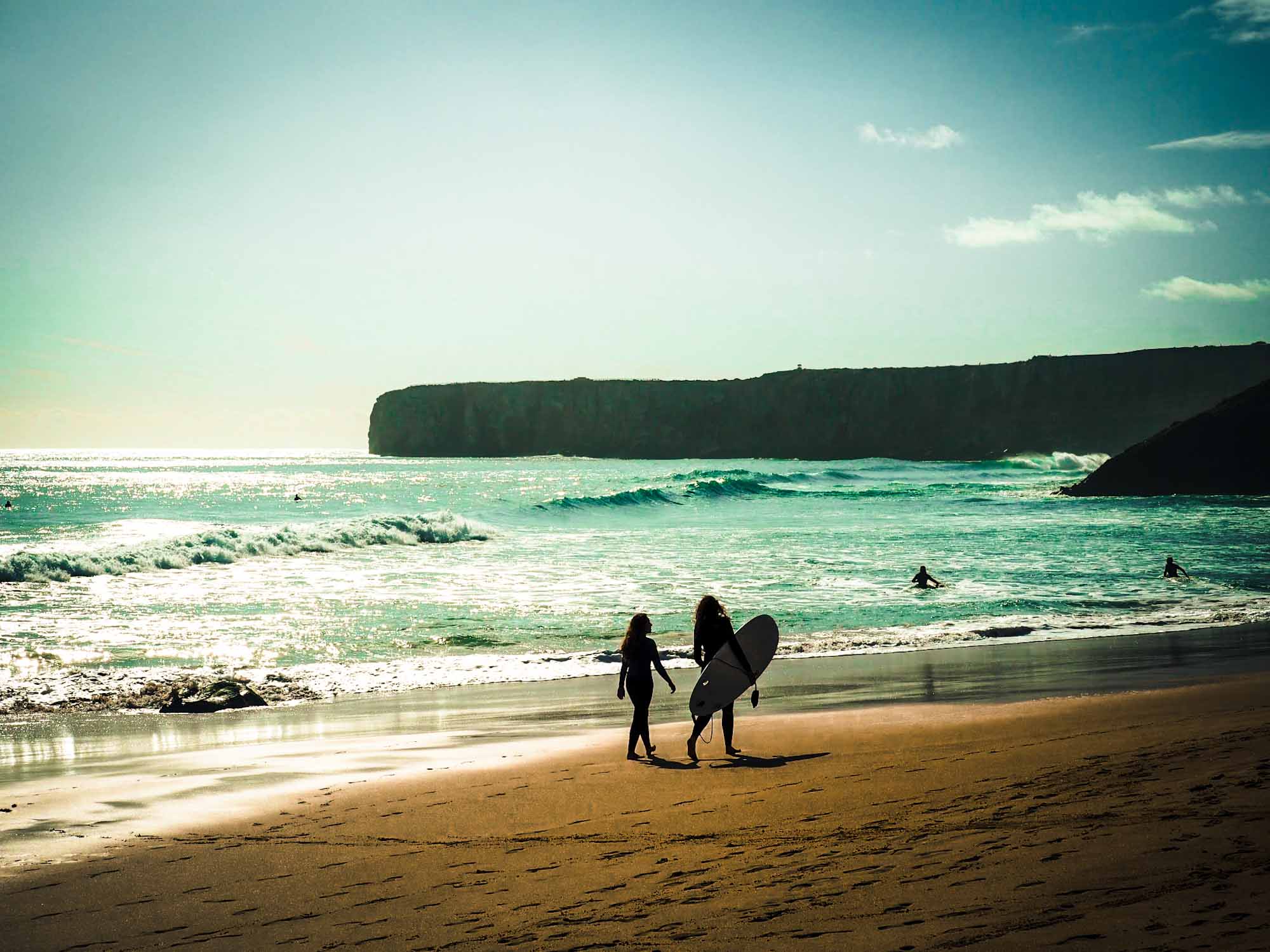 Surfers walking along a sandy beach with waves in the sea behind