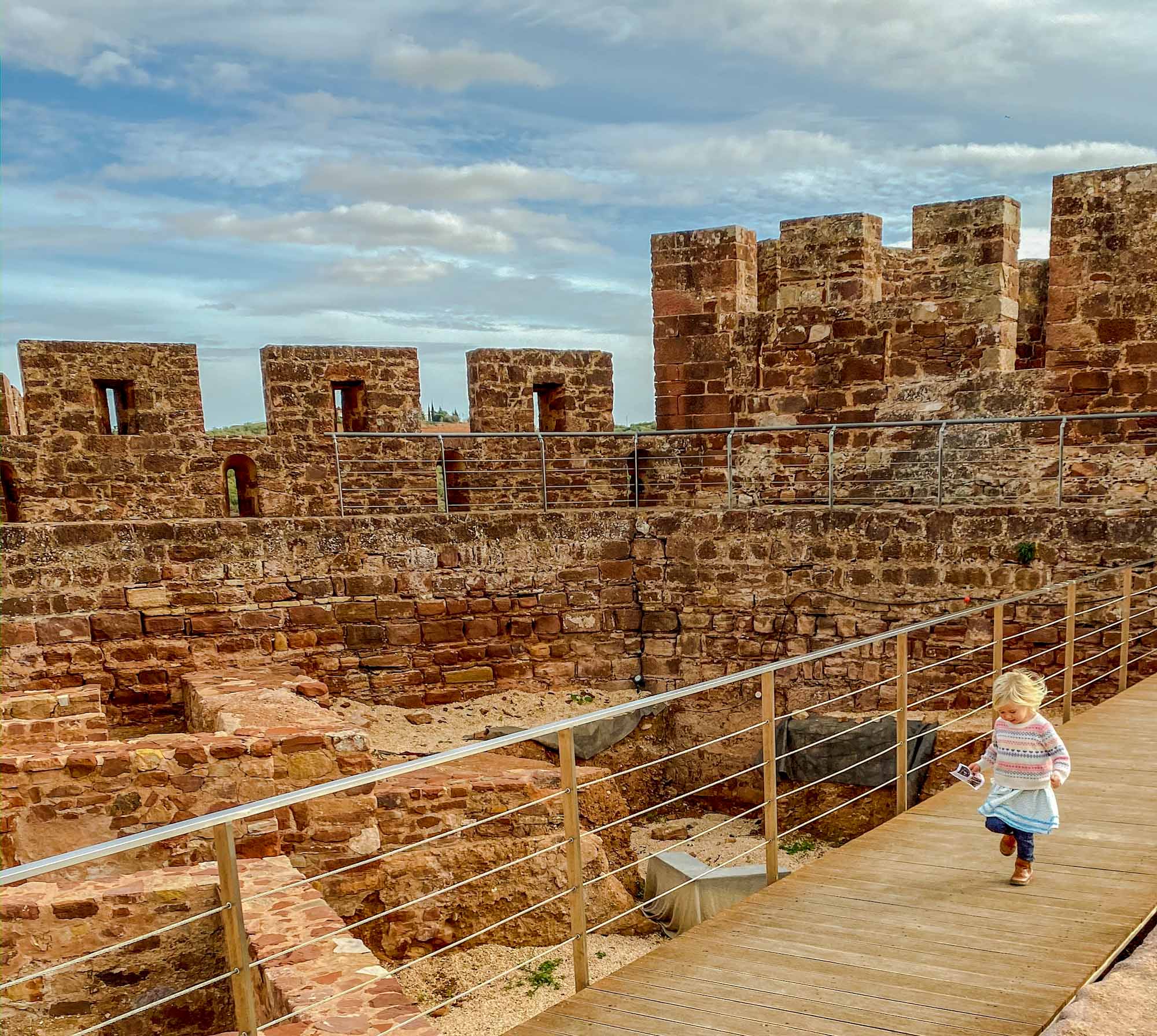 Young girl running along a boardwalk inside castle walls