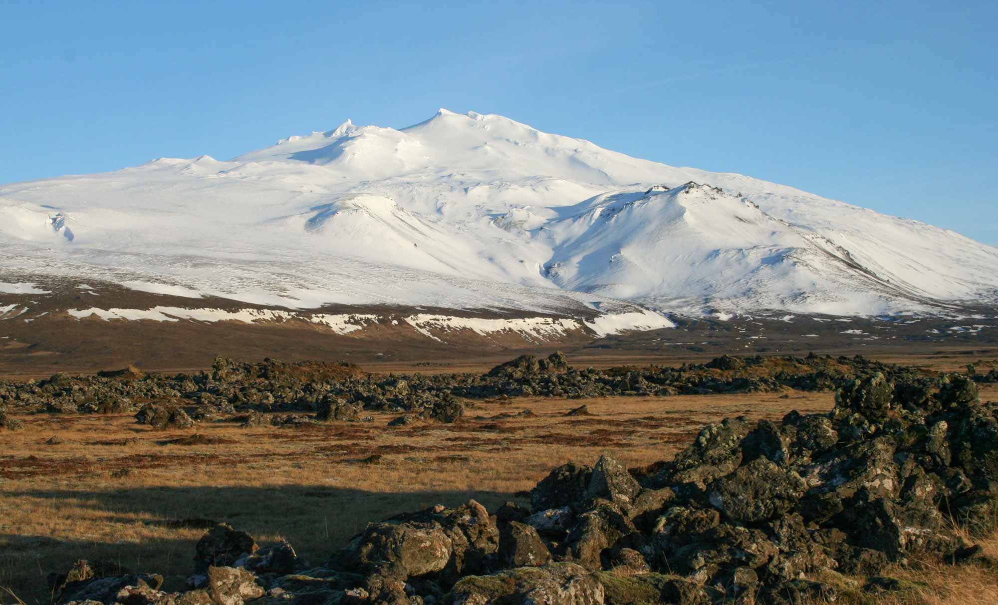 The peak of Snæfellsjökull volcano, Iceland, covered in snow, with granite rocks in the foreground